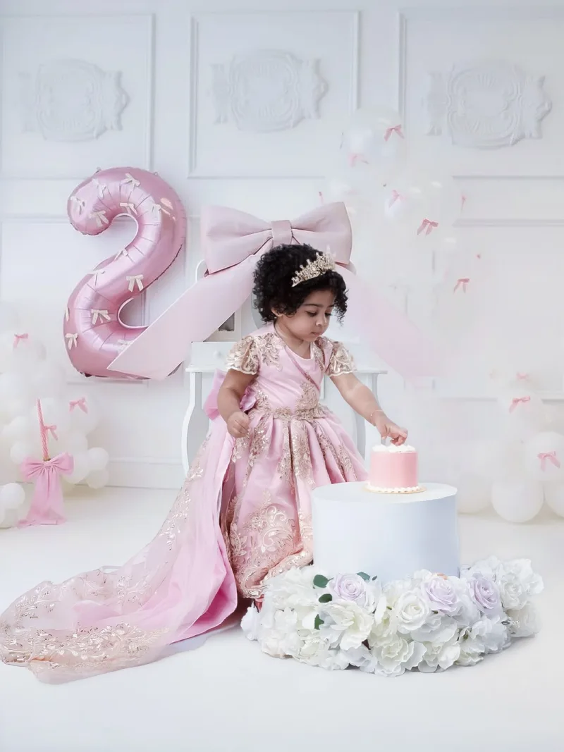 Toddler reaching for her pink birthday cake on a floral stand