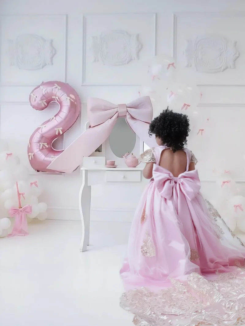 Toddler seen from behind at a white vanity, bow train trailing