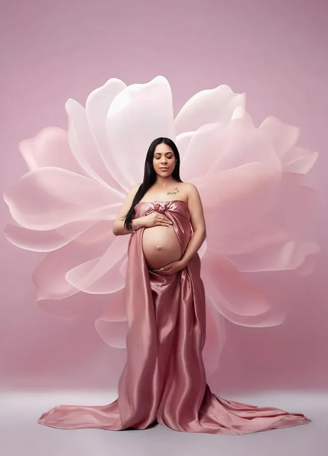 Expecting mother in a rose satin gown before an oversized floral backdrop