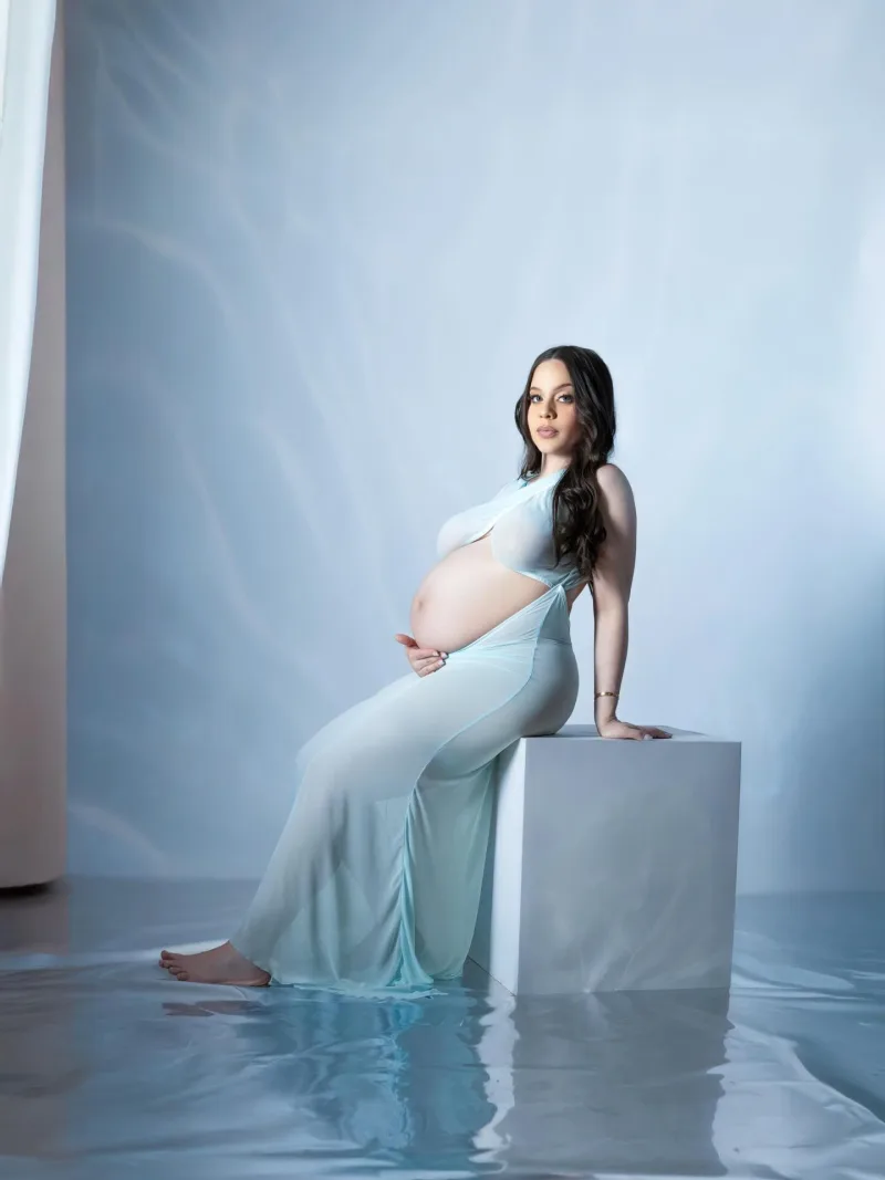Expecting mother seated on a white cube above a mirrored floor