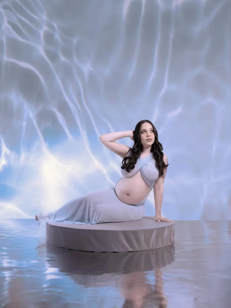 Expecting mother reclining on a podium above rippling water