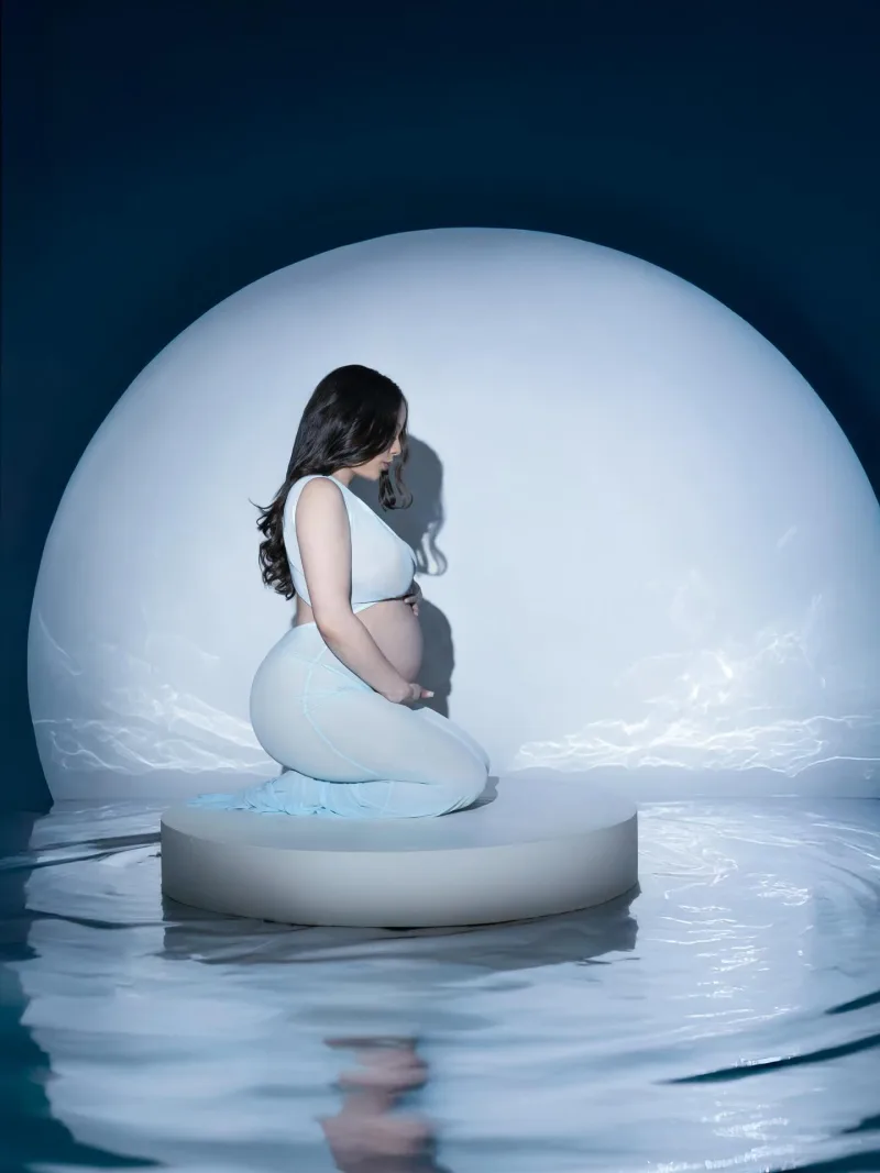 Expecting mother kneeling before a glowing dome above still water