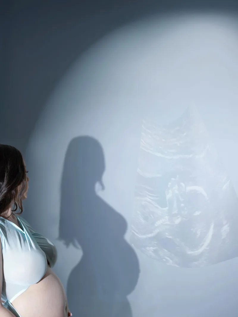 Expecting mother's silhouette beside a projected ultrasound image