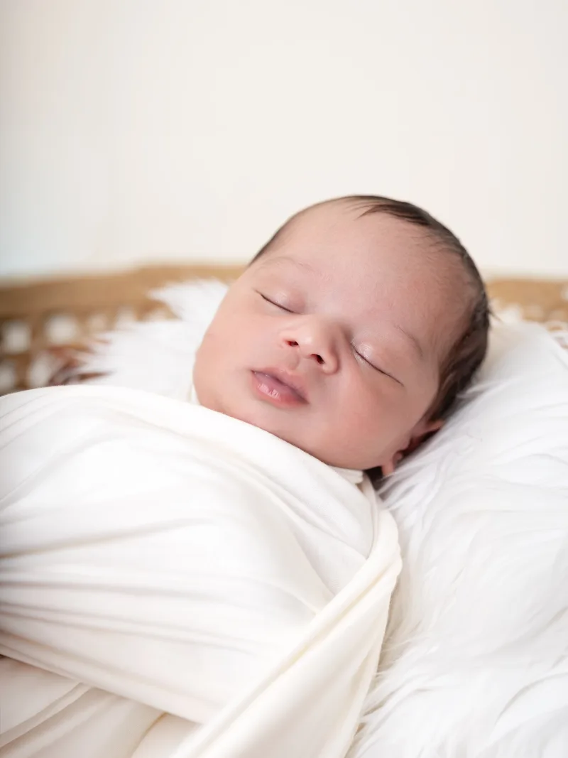 Newborn sleeping in a cream swaddle