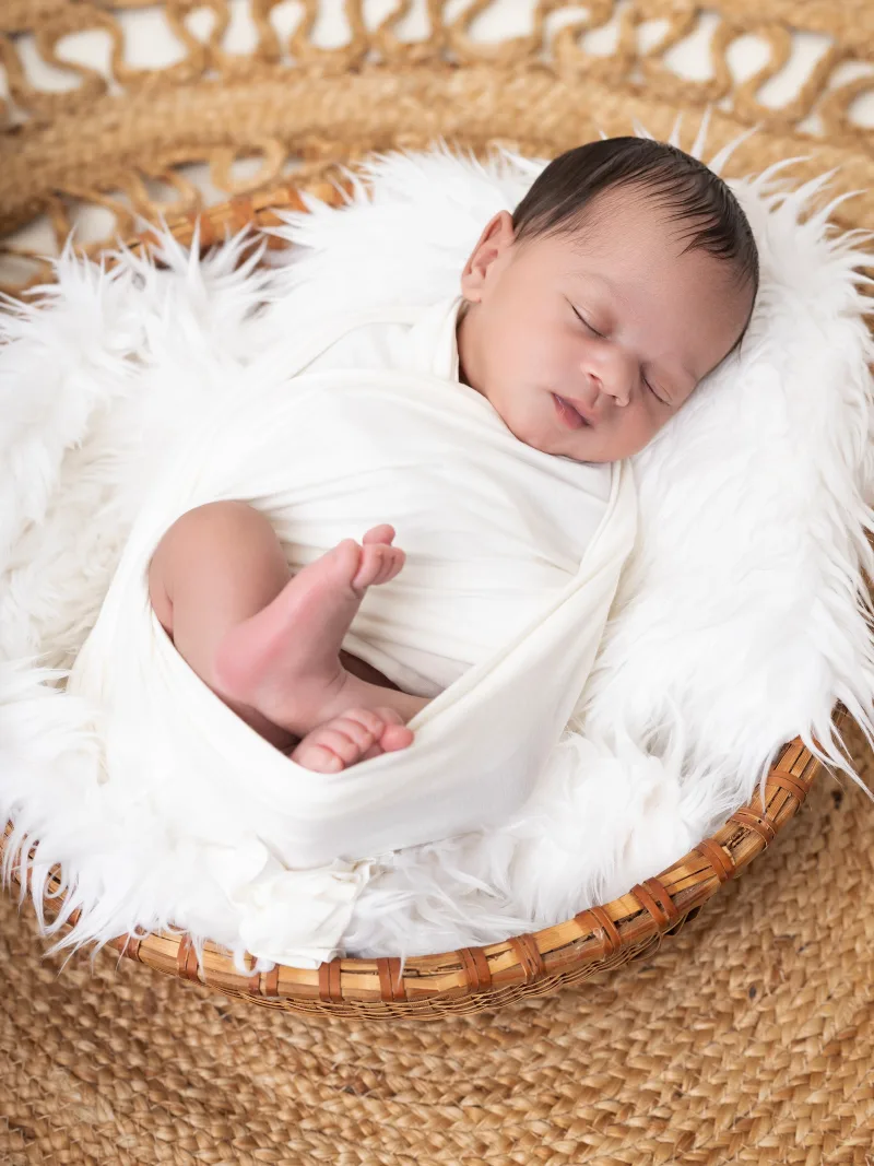 Newborn swaddled in white, photographed from above in a basket