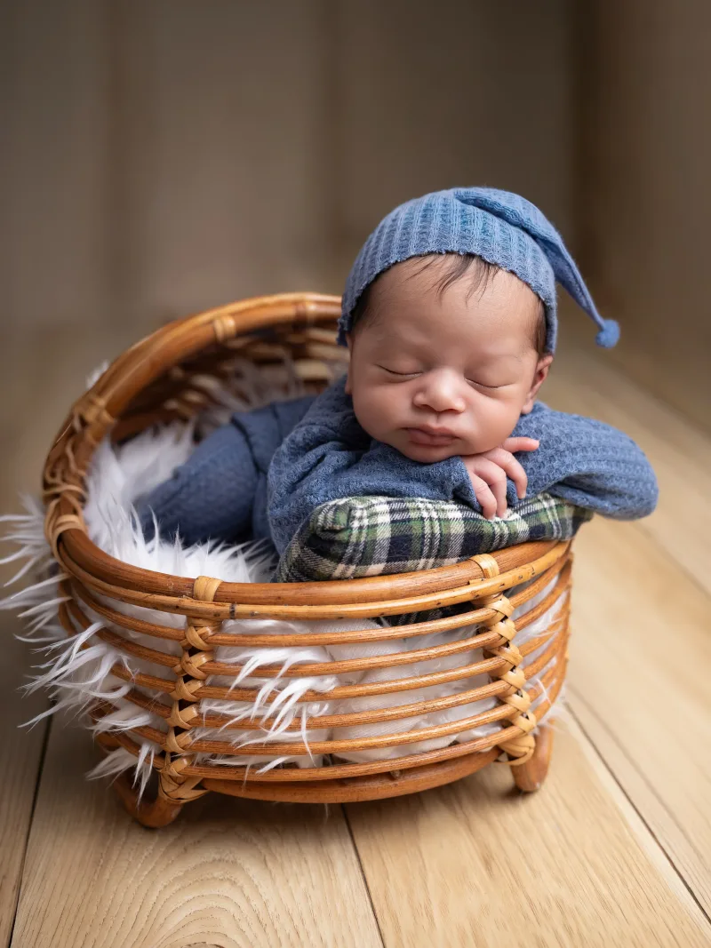 Newborn in a blue knit sleep cap curled in a rattan basket