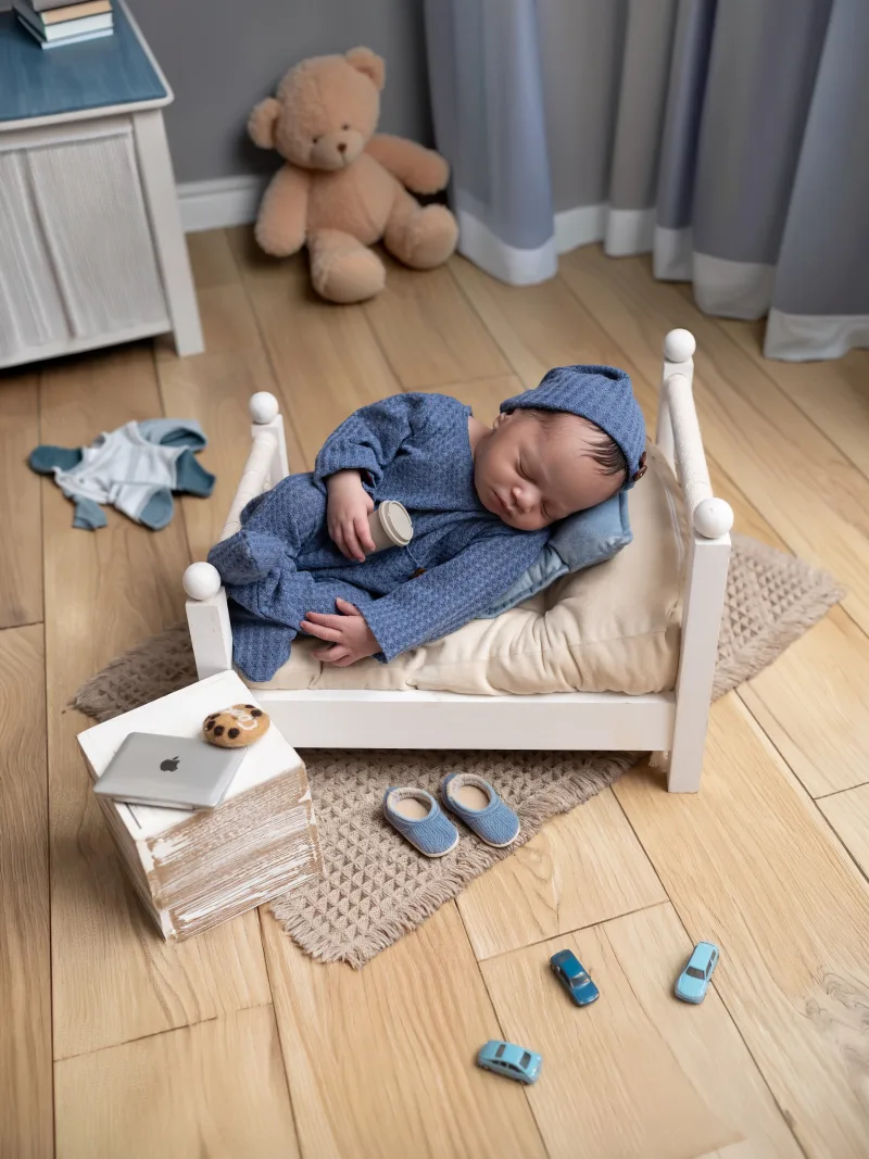Newborn asleep on a miniature bed in a styled nursery set