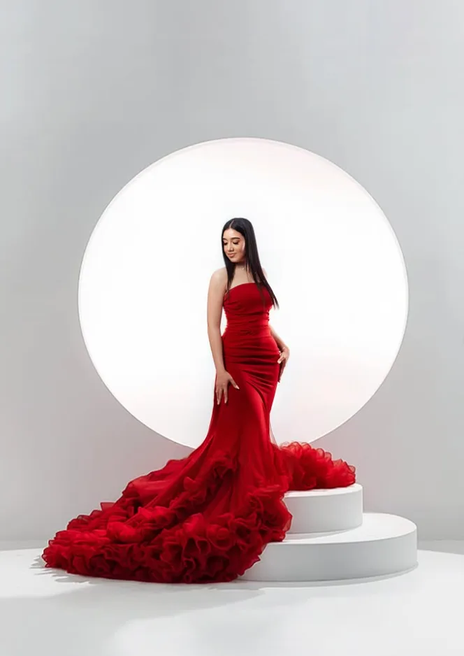 Portrait in a red ruffled gown before a backlit circle